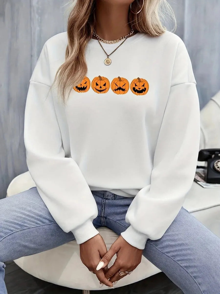 Model sitting casually in a studio setting wearing the white relaxed crewneck sweatshirt with the four jack-o'-lantern pumpkin graphic print, paired with light blue jeans.