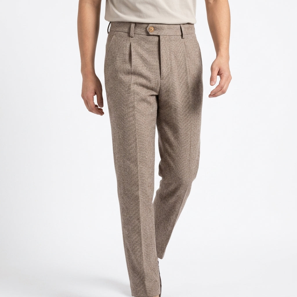 Front view of a man wearing light brown herringbone wool trousers paired with a light-colored crewneck t-shirt against a plain white studio backdrop.