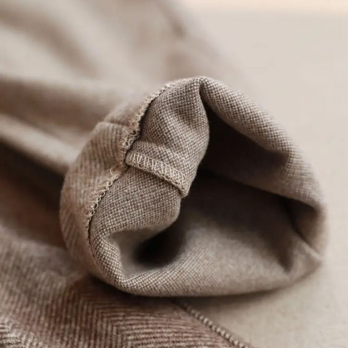 Extreme close-up macro shot showing the internal stitched hem, smooth interior lining, and soft textured wool weave of the trousers.