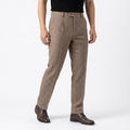 Front three-quarter view of a man wearing beige herringbone wool trousers with a pleated front, tailored fit, slant pockets, and brown dress shoes, paired with a black t-shirt against a white background.