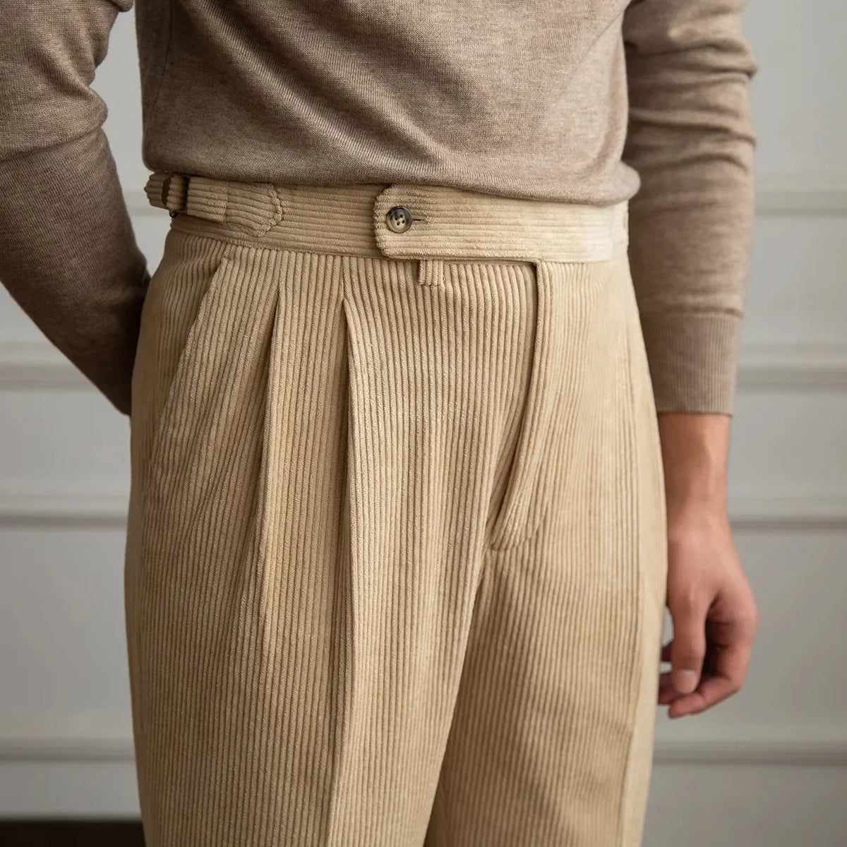 Close-up of beige pleated corduroy pants showing the waistband and side adjuster