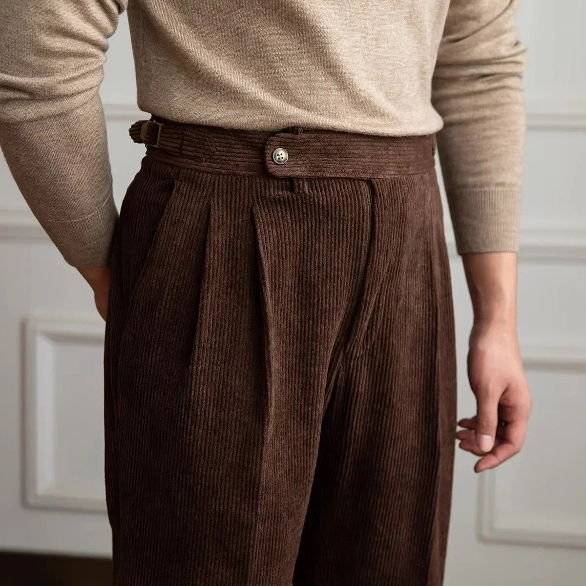 Close-up of brown pleated corduroy pants showing the high waistband and side adjuster