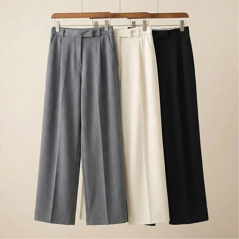 Three pairs of high-waisted wide-leg wool trousers in gray, cream, and black displayed together on wooden clothing hangers.