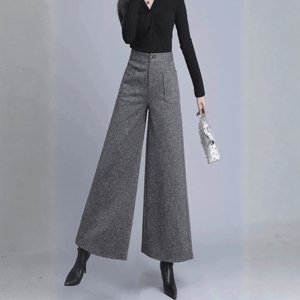 Full-length front view of a model wearing high-waisted gray wide-leg wool pants, holding a small white handbag.