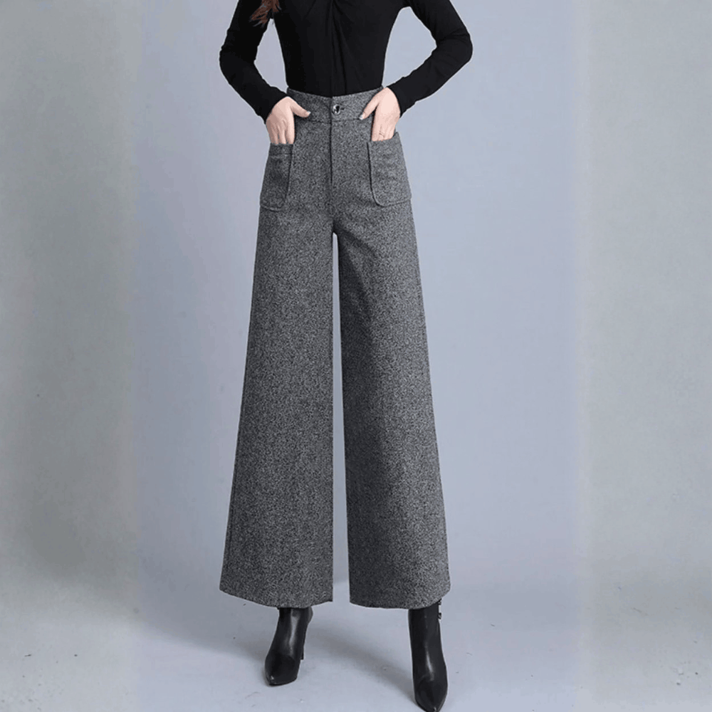 Front view of a model wearing high-waisted gray tweed-wool wide-leg trousers with front welt pockets, paired with a black long-sleeve top and black boots.