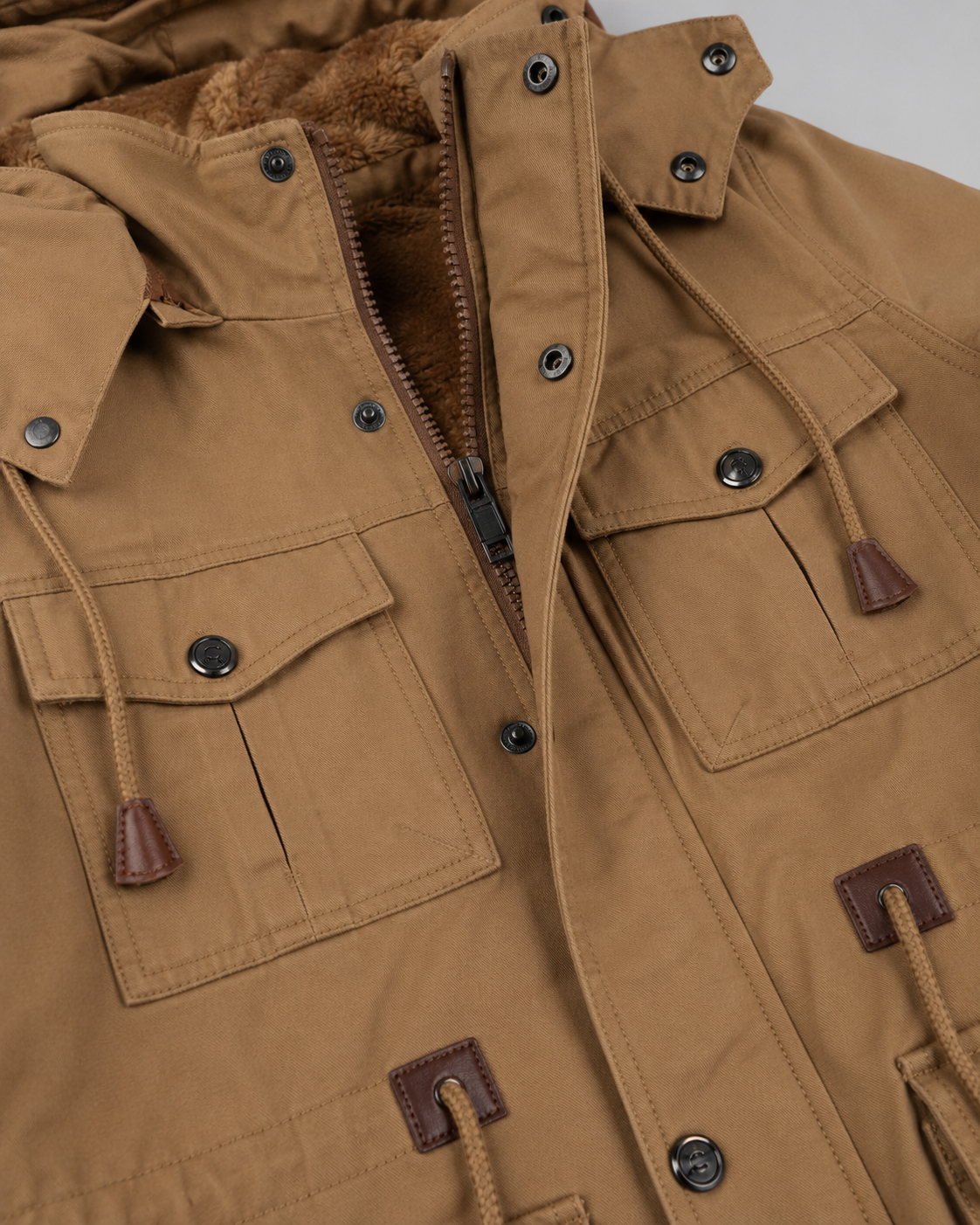 Close-up detail view of the open zipper, fleece lining, dual chest flap pockets, and adjustable drawstrings on the tan utility jacket.