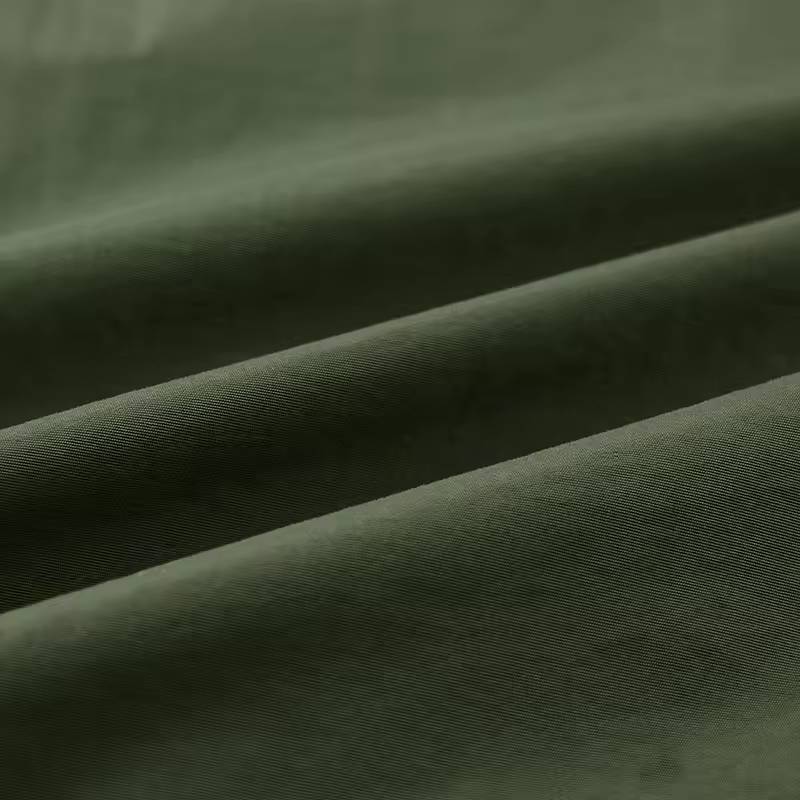 Close-up macro shot showing the woven fabric texture and fold details of the green utility jacket material.