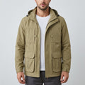 Front view of a model wearing an open beige utility jacket with an attached hood, stand collar, front zip closure, dual chest flap pockets, and dual lower cargo flap pockets over a white t-shirt.