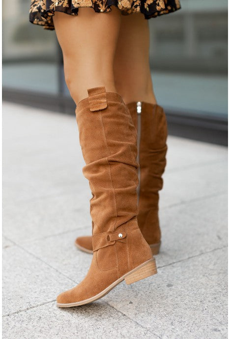 Camel slouch knee-high suede boots featuring pointed toes, side buckle detail, and block heels, worn outdoors.
