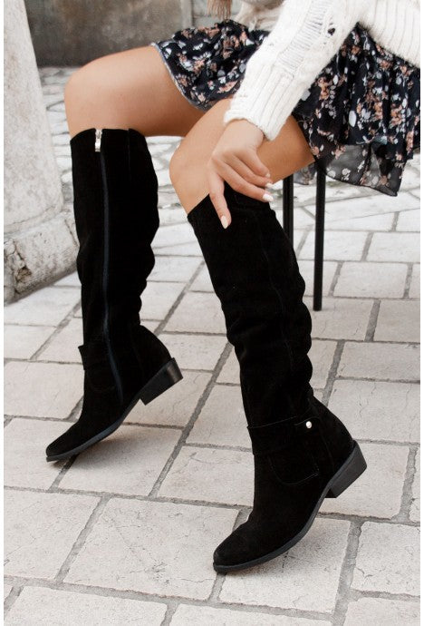 Black slouch knee-high suede boots with pointed toes, side buckle detail, and block heels, styled with a floral dress.