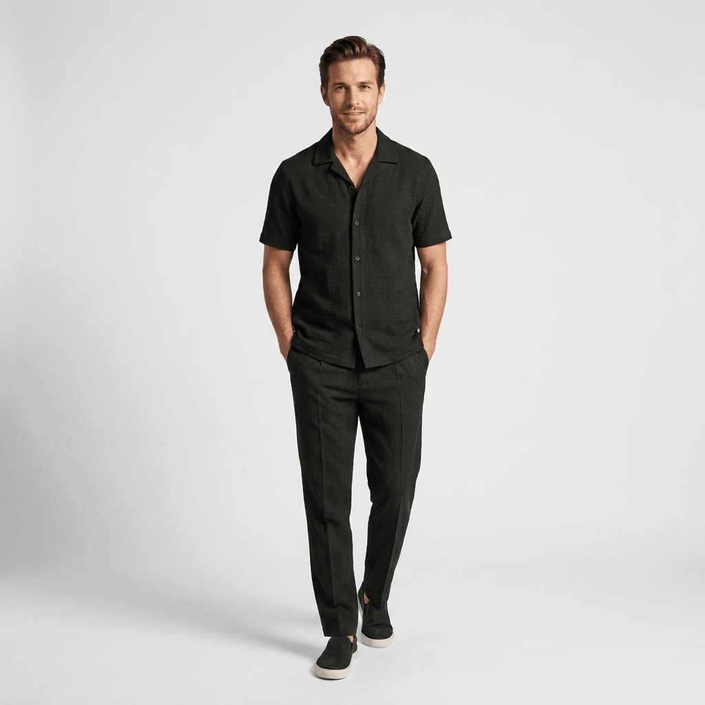 Man wearing a black short-sleeve linen shirt with matching black linen trousers and white sneakers.