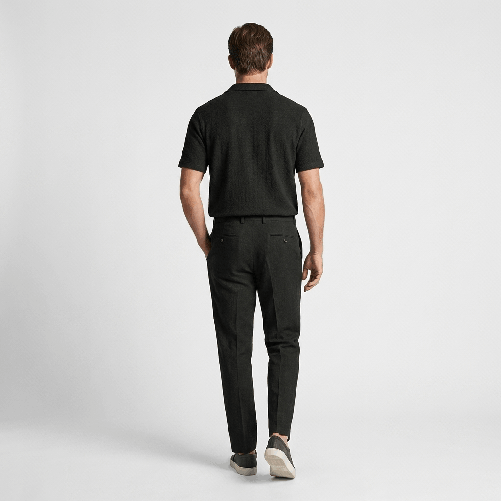 Back view of a man wearing a black short-sleeve linen shirt with matching black linen trousers.