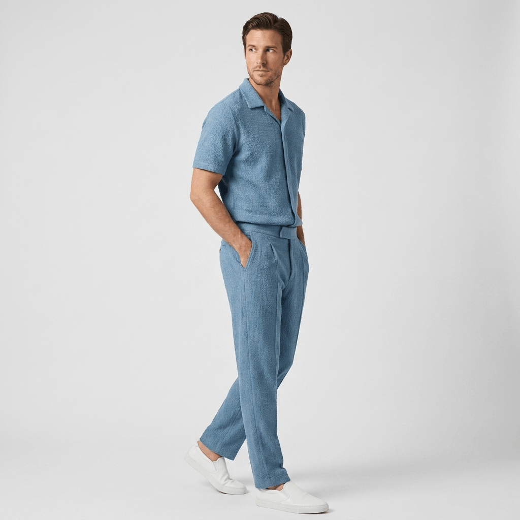 Side view of a man wearing a light blue short-sleeve linen shirt with matching linen trousers and white sneakers.