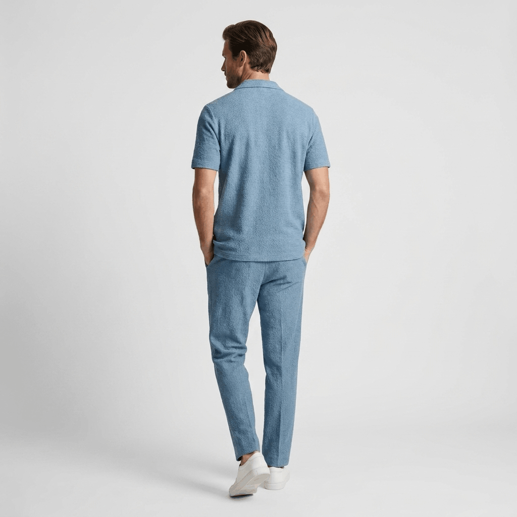 Back view of a man wearing a light blue short-sleeve linen shirt with matching linen trousers.