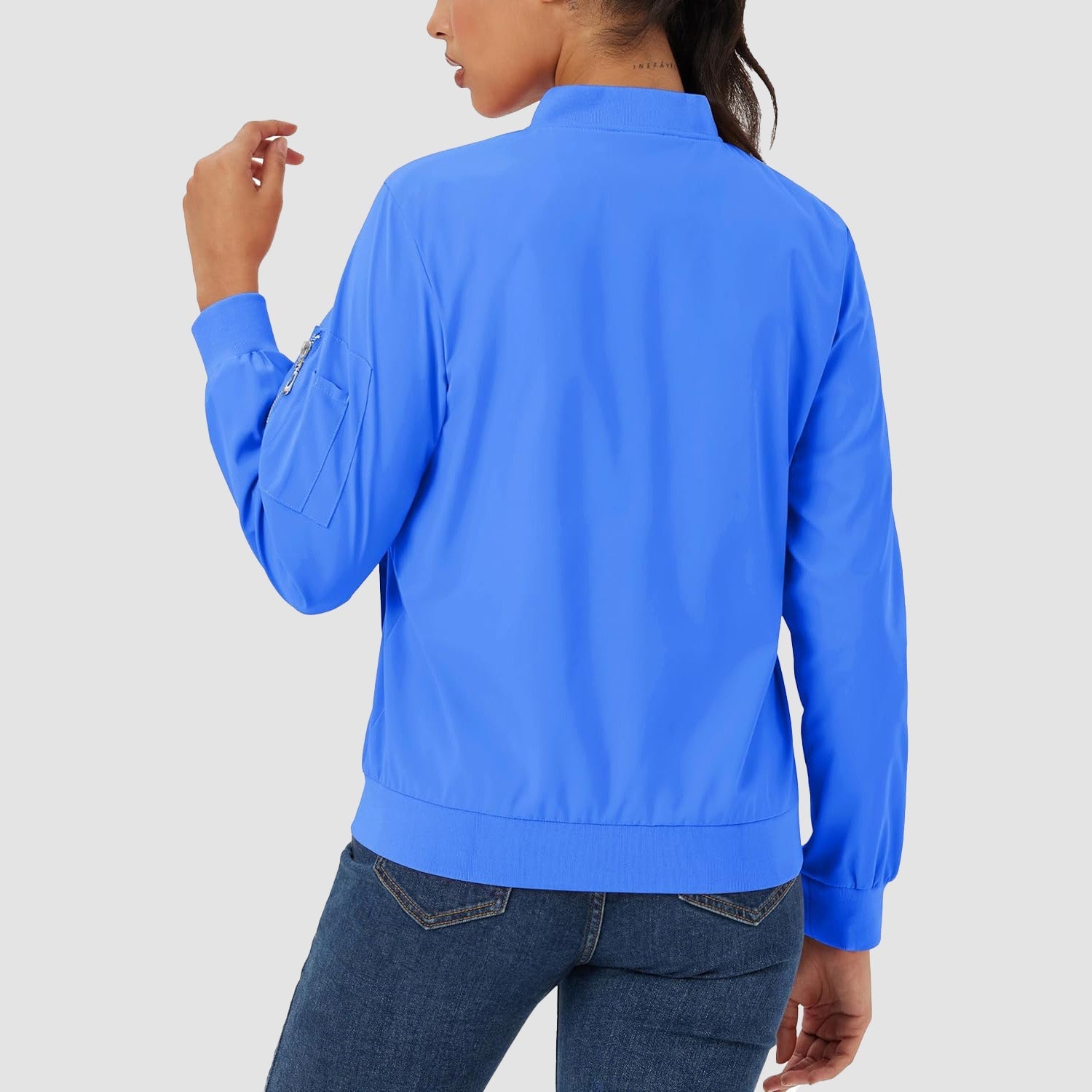 Bright blue lightweight bomber jacket with ribbed trim and a zip sleeve pocket, worn over dark denim jeans.