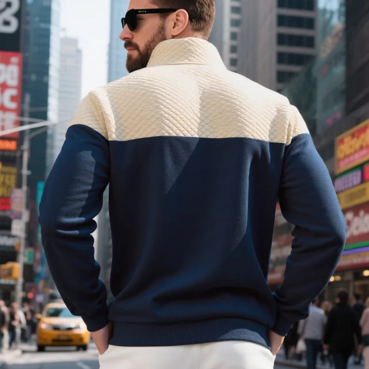 Back view of a navy and beige color-block quarter-zip fleece pullover, styled with white trousers on a city street.