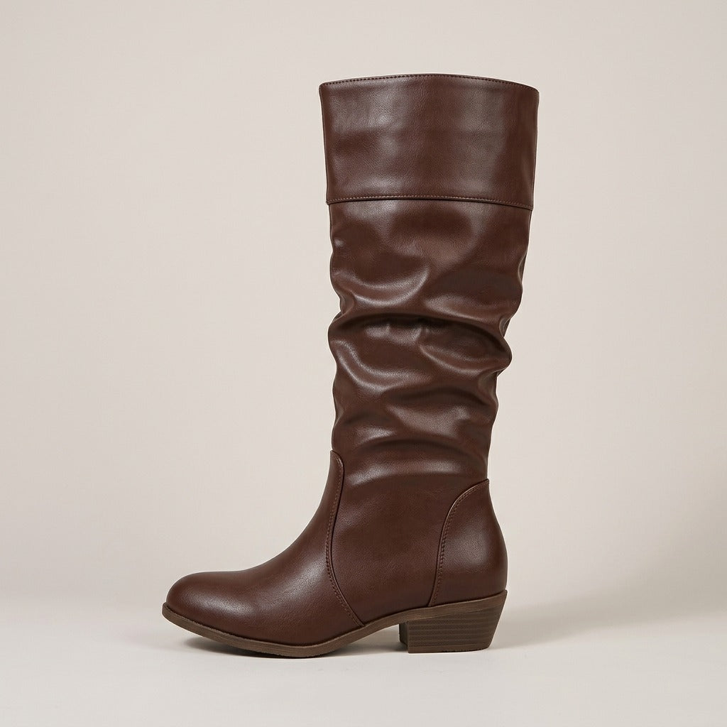 Brown knee-high riding boots in smooth faux leather with a slouchy shaft, cuffed top band, and low stacked heel.