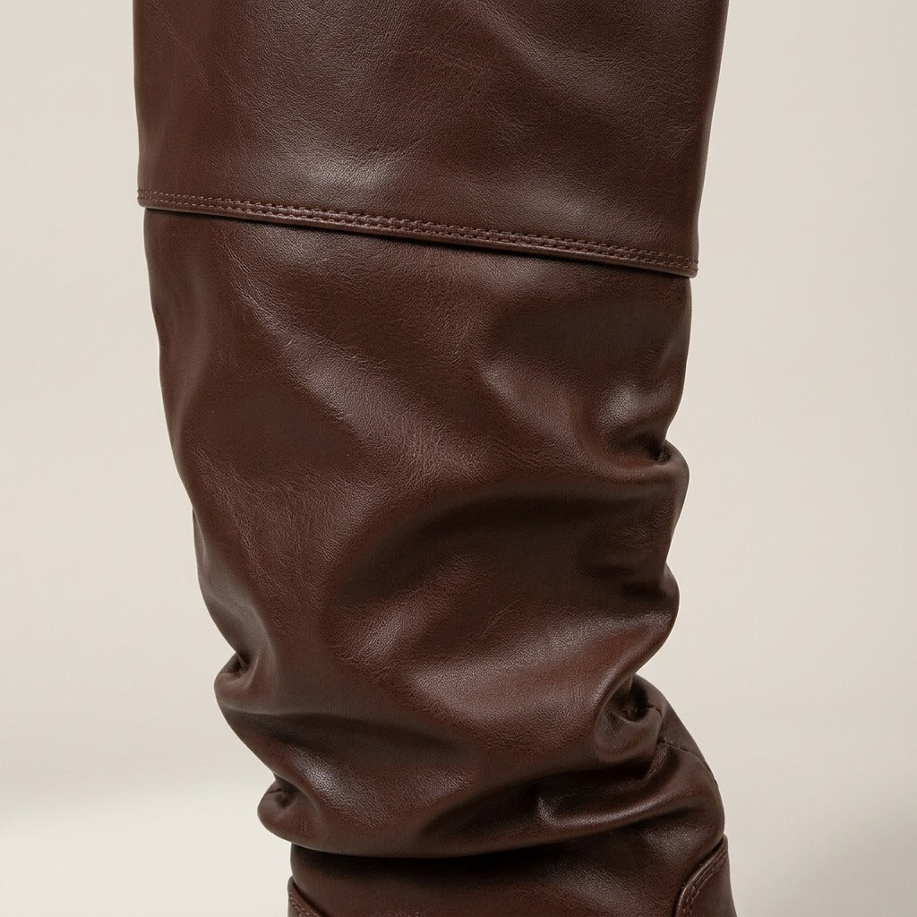 Brown knee-high riding boots in smooth leather-look material featuring a relaxed slouchy shaft and cuffed top band.