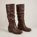 Brown knee-high riding boots in smooth faux leather with a slouchy shaft, cuffed top, and low stacked wood-look heel.