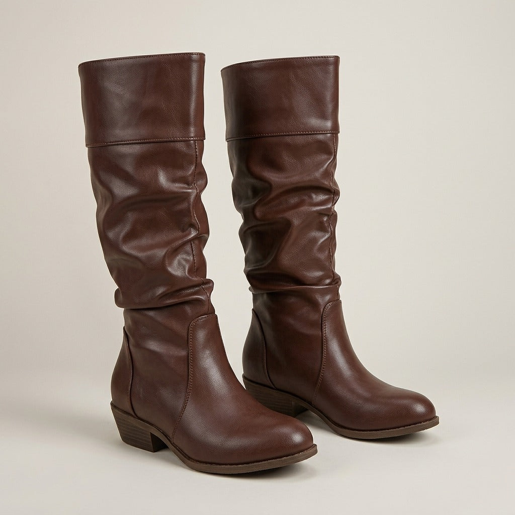 Brown knee-high riding boots in smooth faux leather with a slouchy shaft, cuffed top, and low stacked wood-look heel.