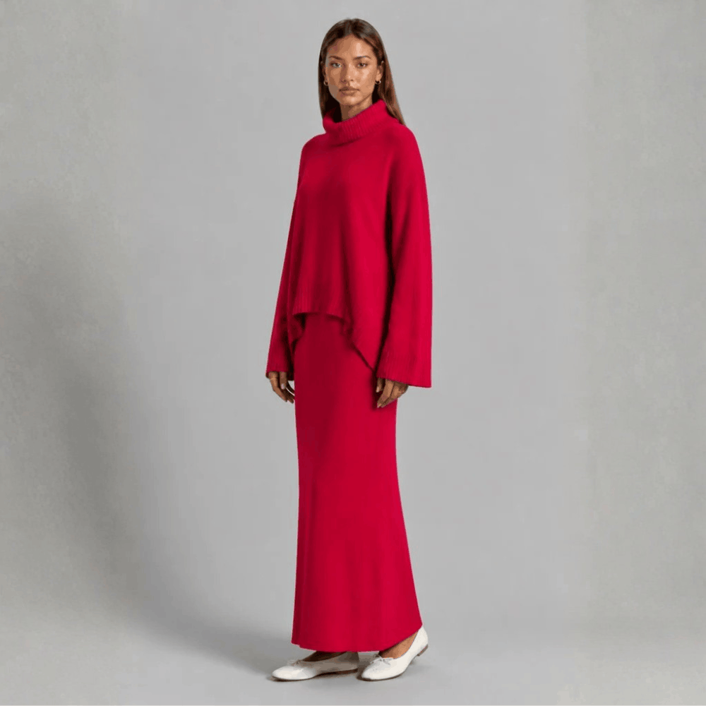 Three-quarter front view of a model wearing the bright red oversized turtleneck knit sweater and long maxi skirt co-ord set.