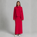 Full-length front view of a model wearing a bright red knit two-piece set featuring an oversized turtleneck sweater with dropped shoulders and a matching column maxi skirt, styled with white ballet flats.