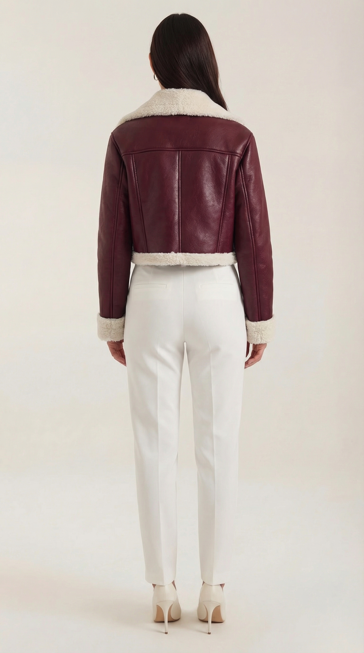 Burgundy leather aviator jacket with plush cream shearling trim, cropped fit, and fleece lining worn over white trousers.