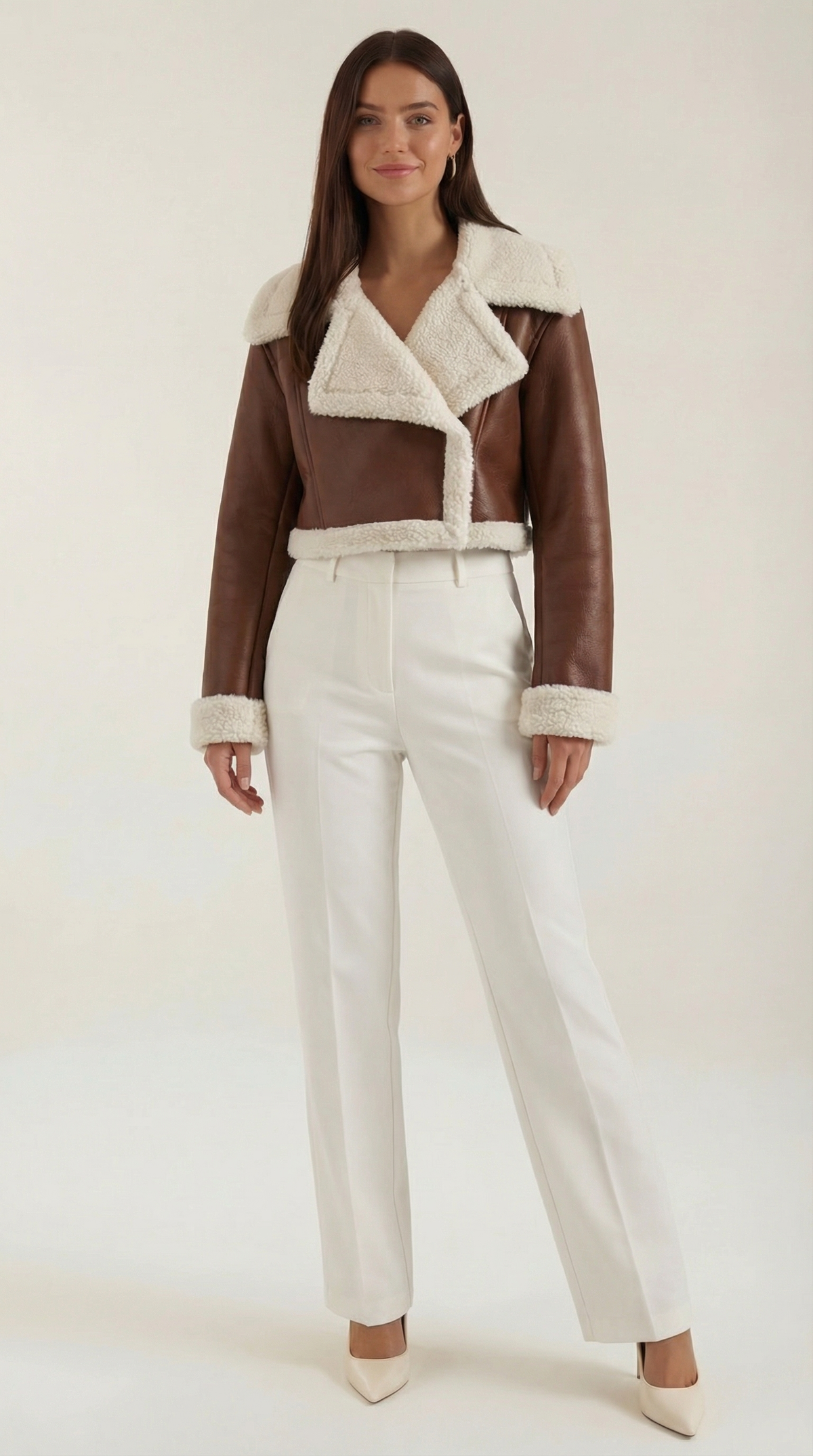 Brown leather aviator jacket with plush white shearling trim, featuring a cropped fit worn with white trousers.