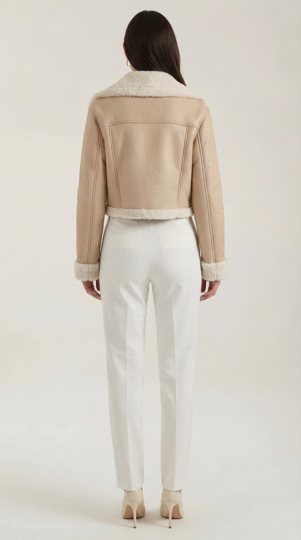 Beige cropped leather aviator jacket with plush shearling trim on the collar, cuffs, and hem, worn with white trousers.
