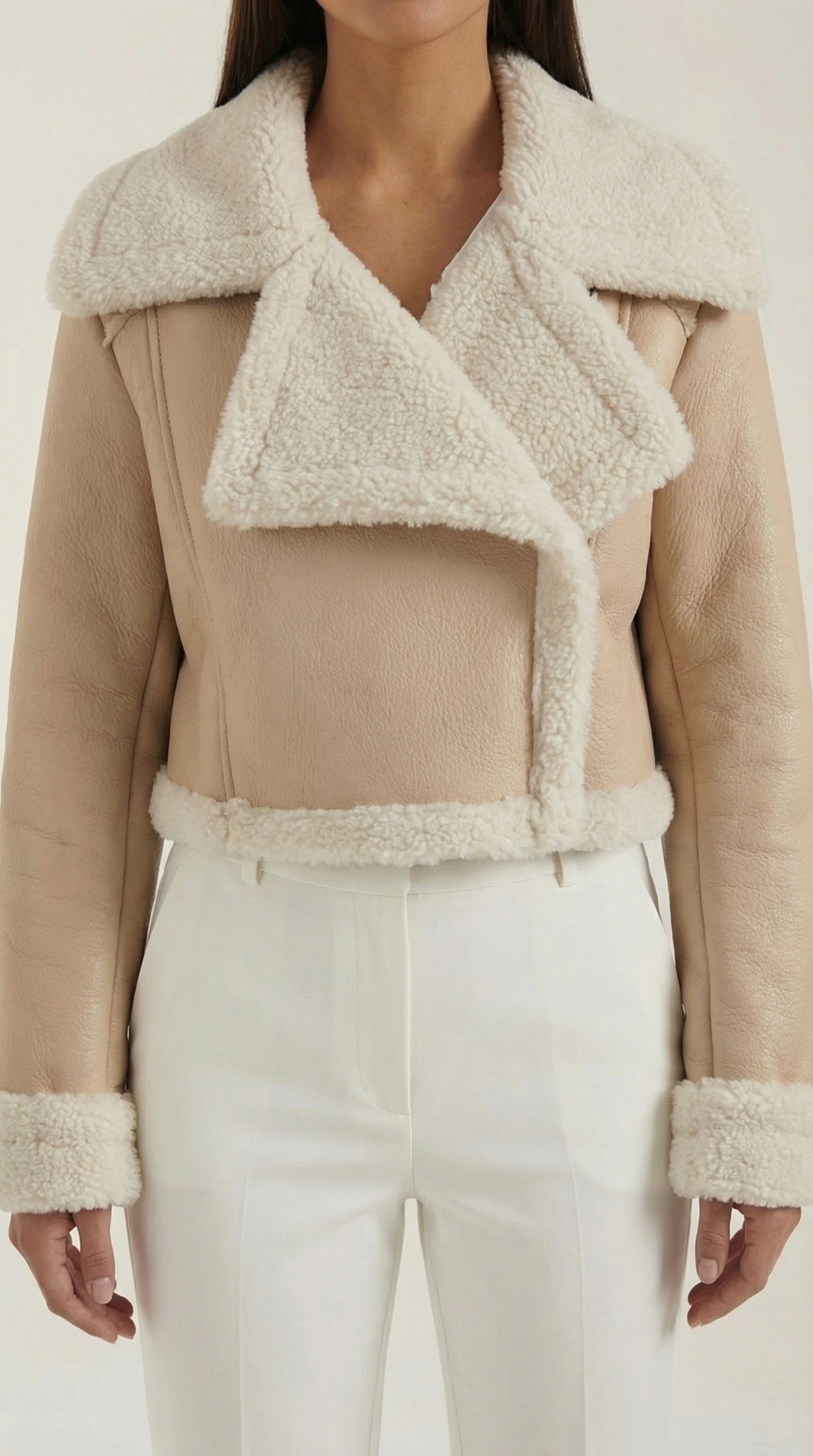 Beige leather aviator jacket with a cropped fit, plush shearling collar, and fleece-lined cuffs worn with white trousers.