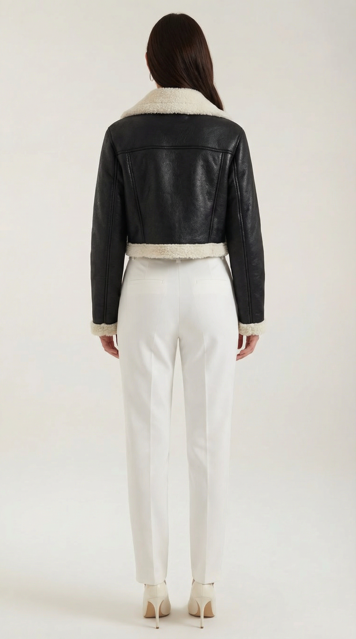 Black leather aviator jacket with a cropped fit, white shearling trim, and fleece lining worn with white trousers.