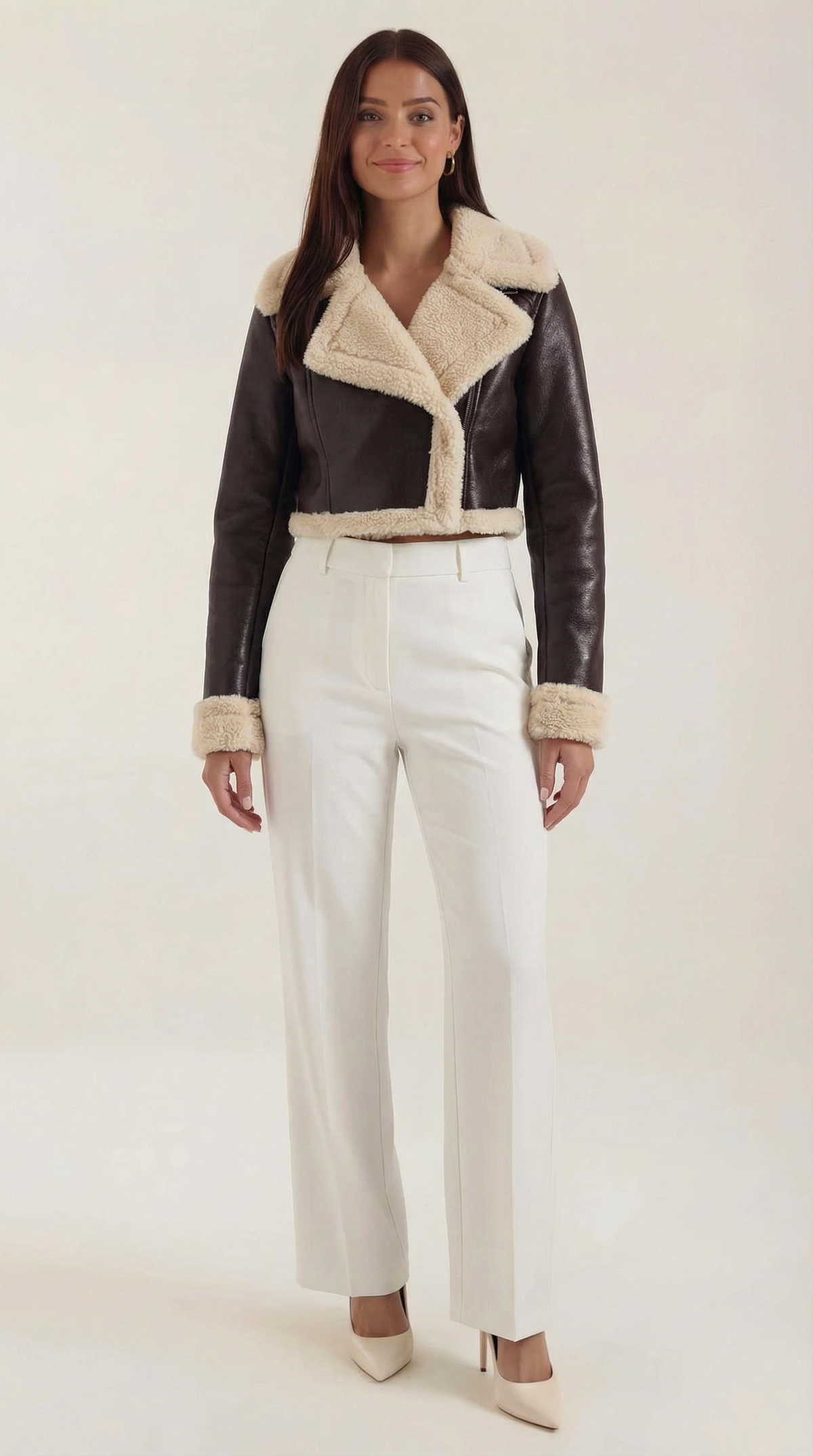 Brown leather aviator jacket with a cropped fit, plush cream shearling trim, and zip-up front worn with white trousers.