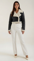 Black cropped leather aviator jacket with plush white shearling trim, worn with tailored white trousers.