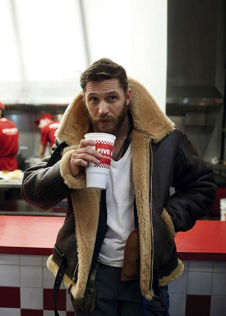 A man wearing a brown leather aviator jacket with shearling lining and a full-zip front, standing indoors