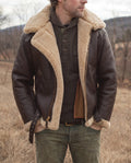 A man wearing a brown leather aviator jacket with shearling lining, a full-zip front, and plush shearling collar