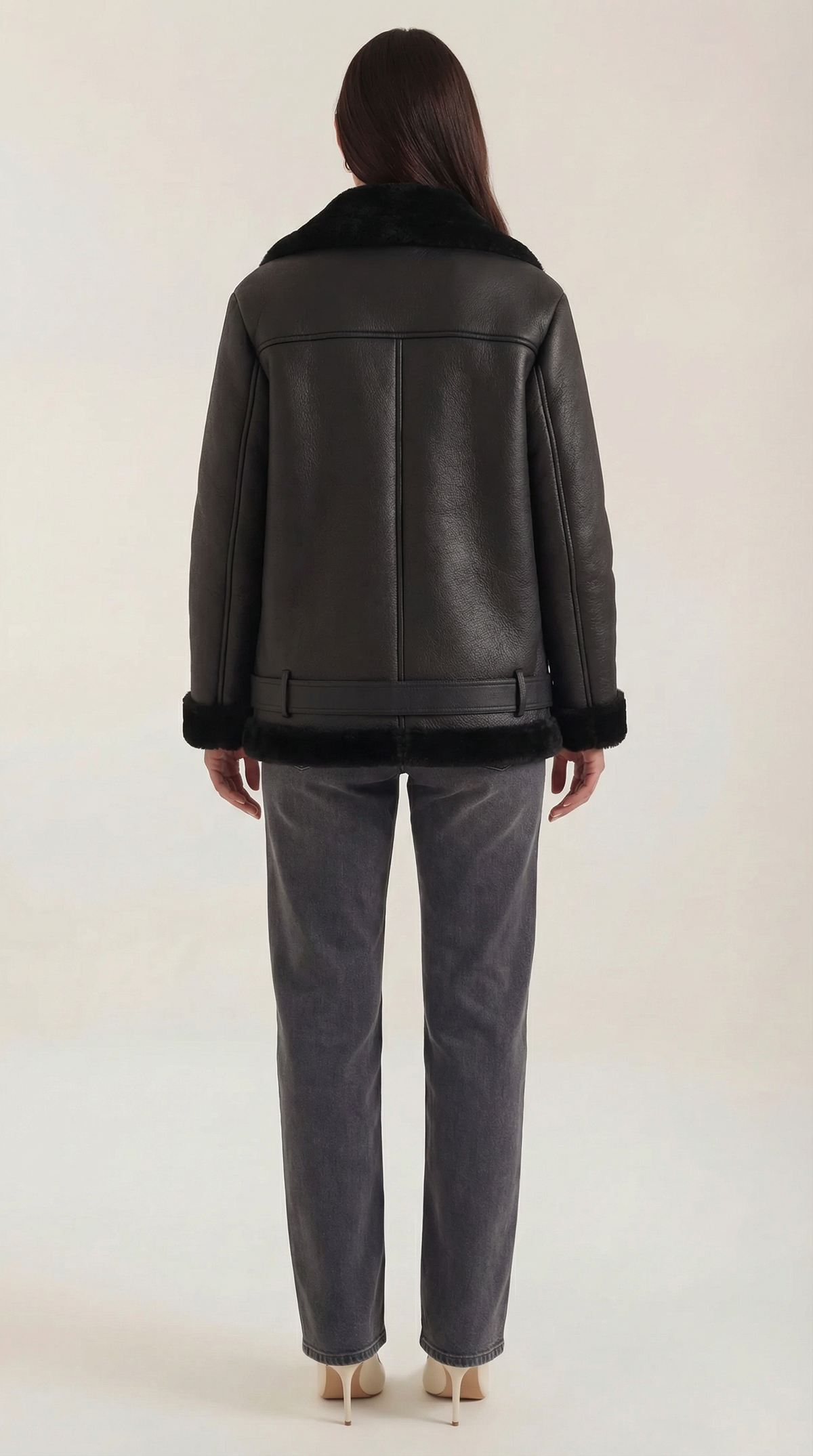 Black leather aviator jacket with shearling collar, cuffs, and belted hem worn over gray jeans.