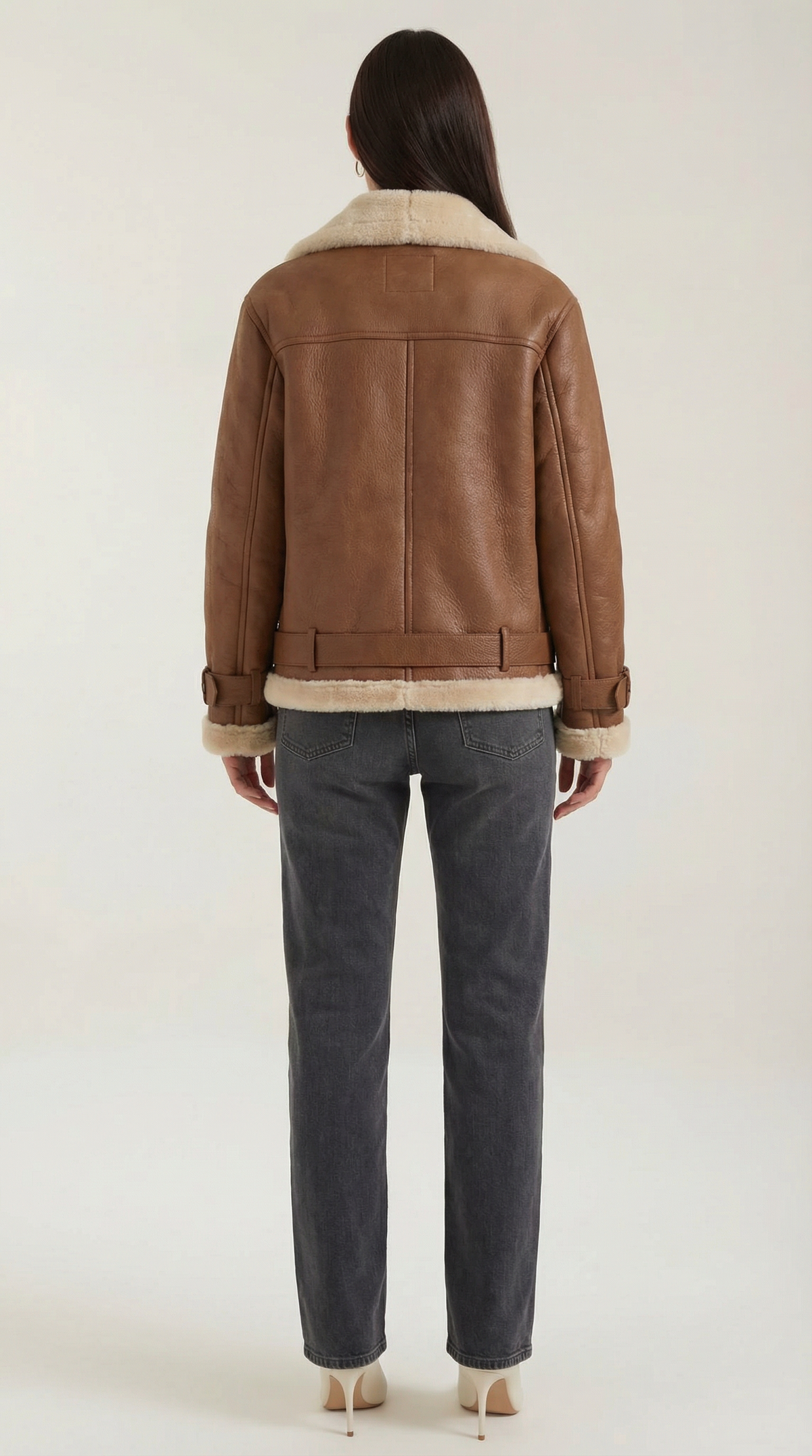 Brown leather aviator jacket with cream shearling trim, belted hem, and structured back view on a model in grey jeans.