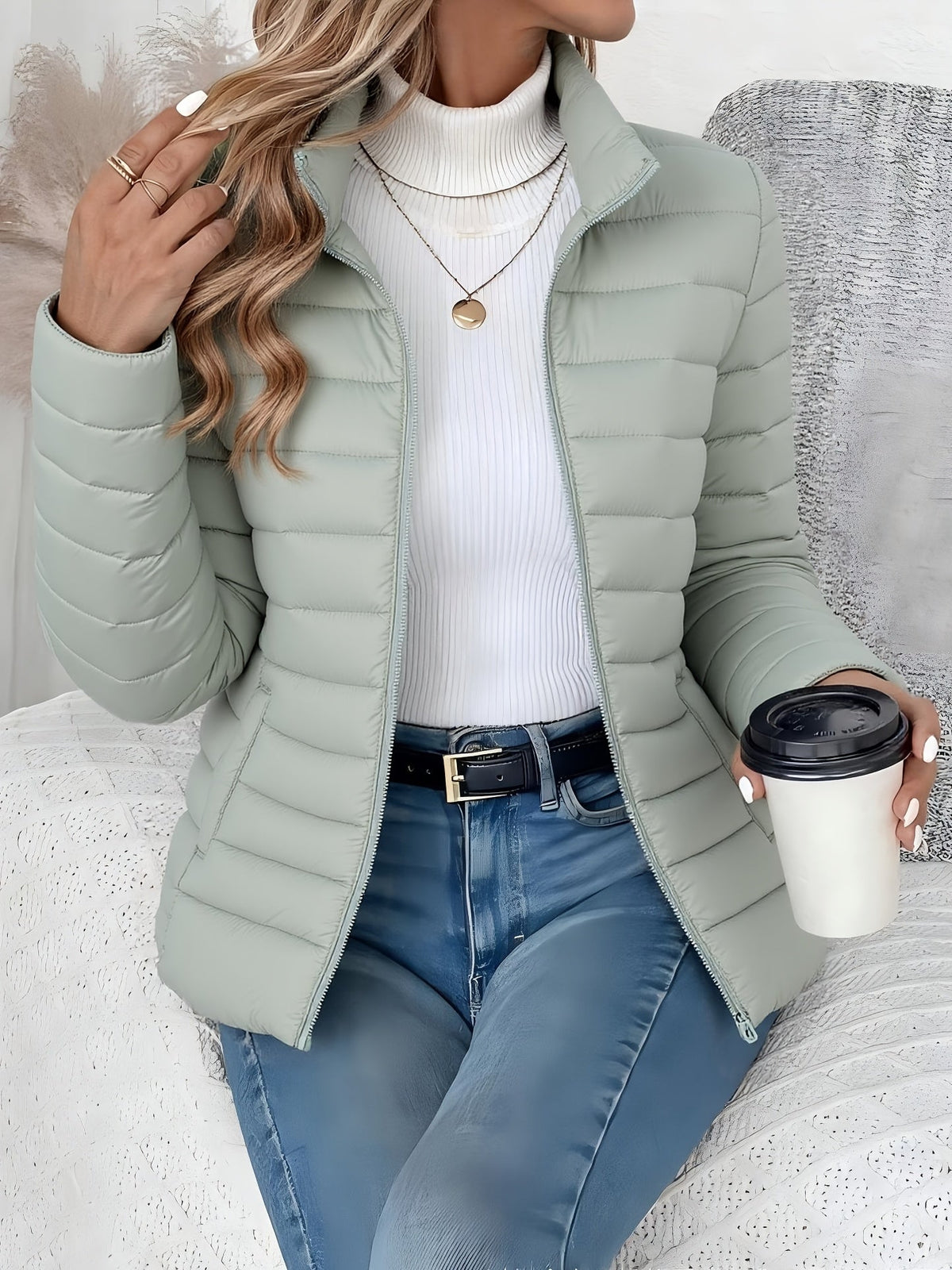 Sage green slim-fit puffer jacket with horizontal channel quilting, stand collar, and zip front worn over a white turtleneck.