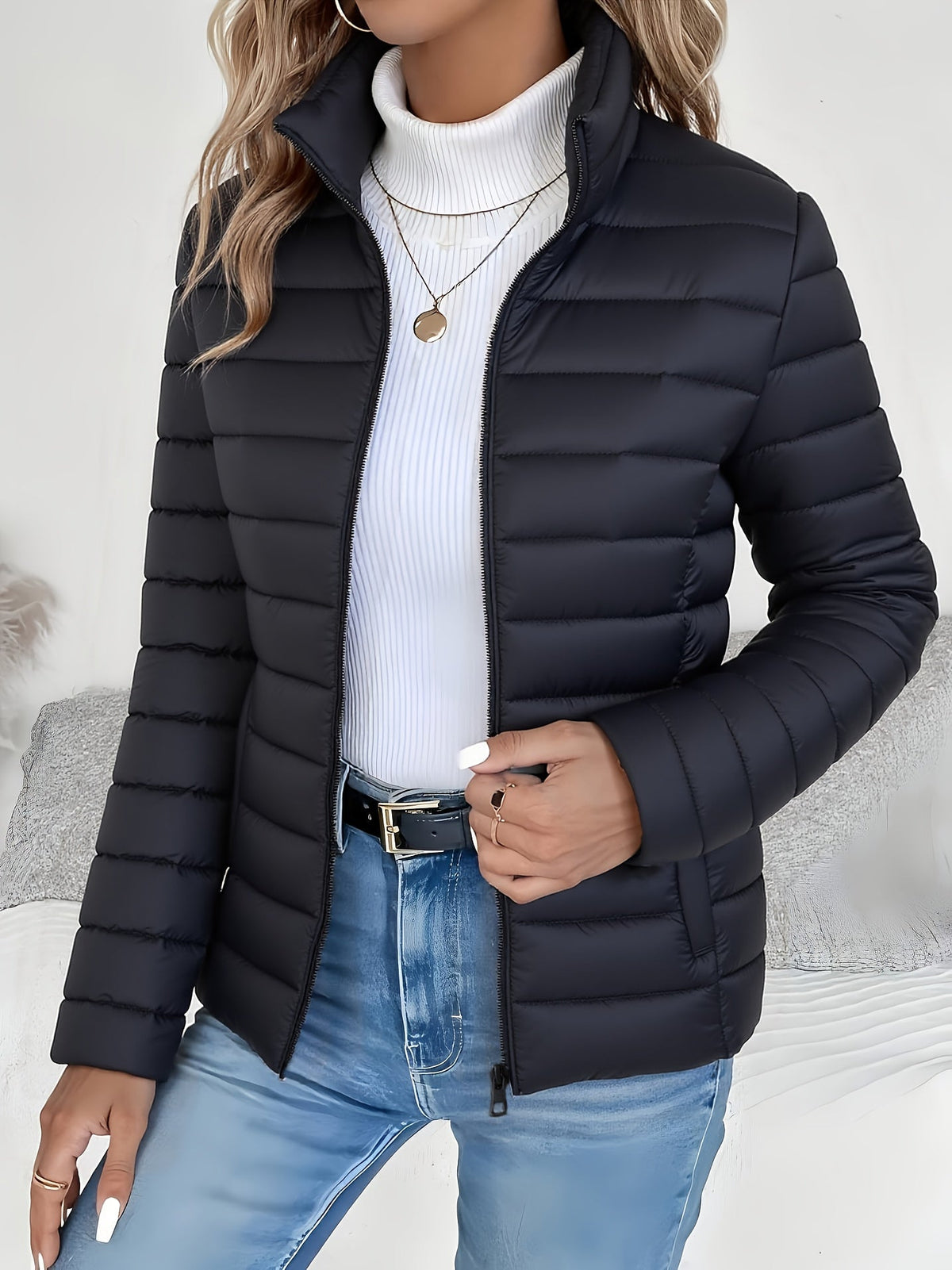 Black slim-fit puffer jacket with horizontal channel quilting, stand collar, and full zip front worn over a white turtleneck.