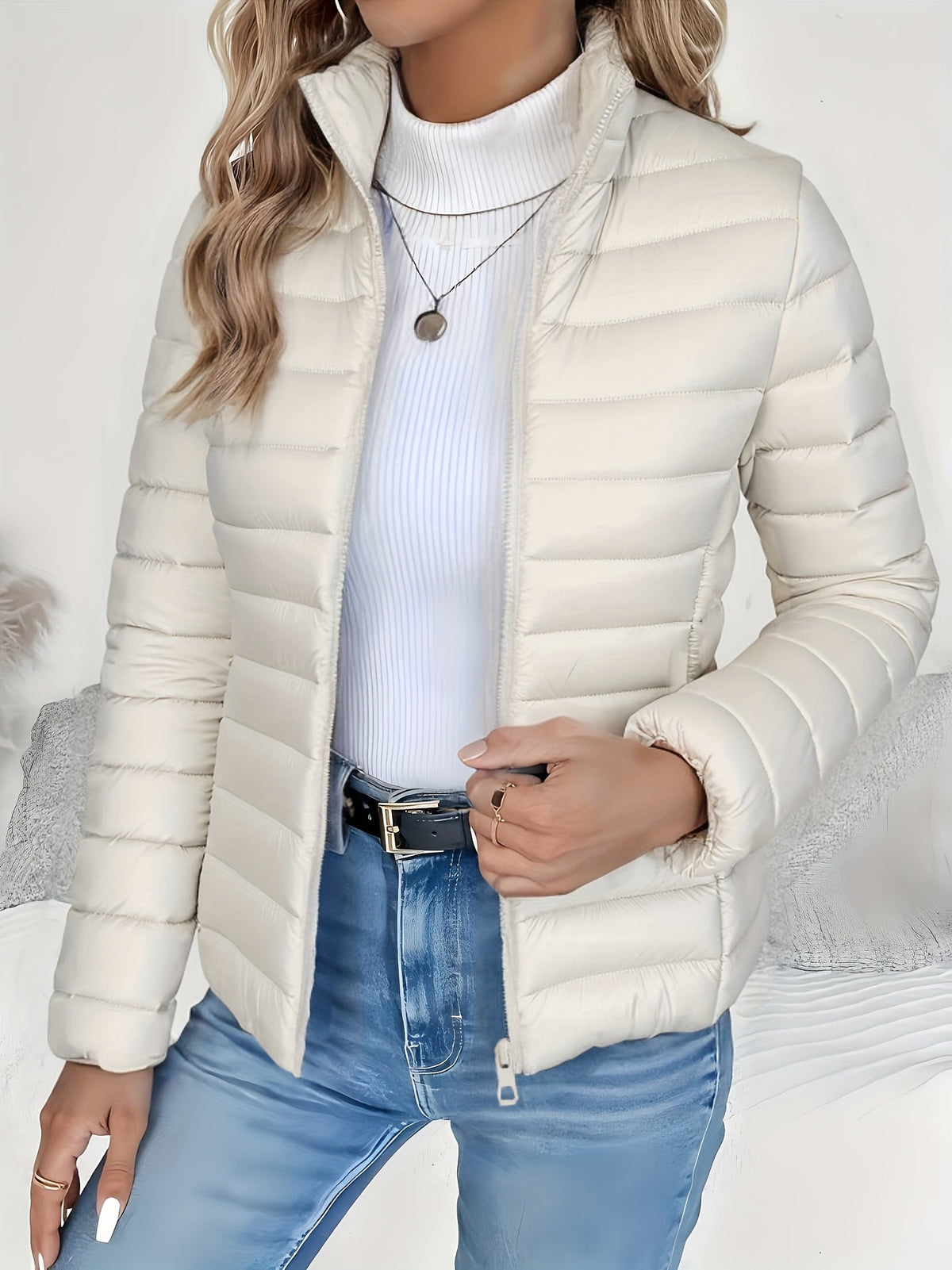 Cream lightweight puffer jacket with slim channel quilting, stand collar, and full zip front worn over a white turtleneck.