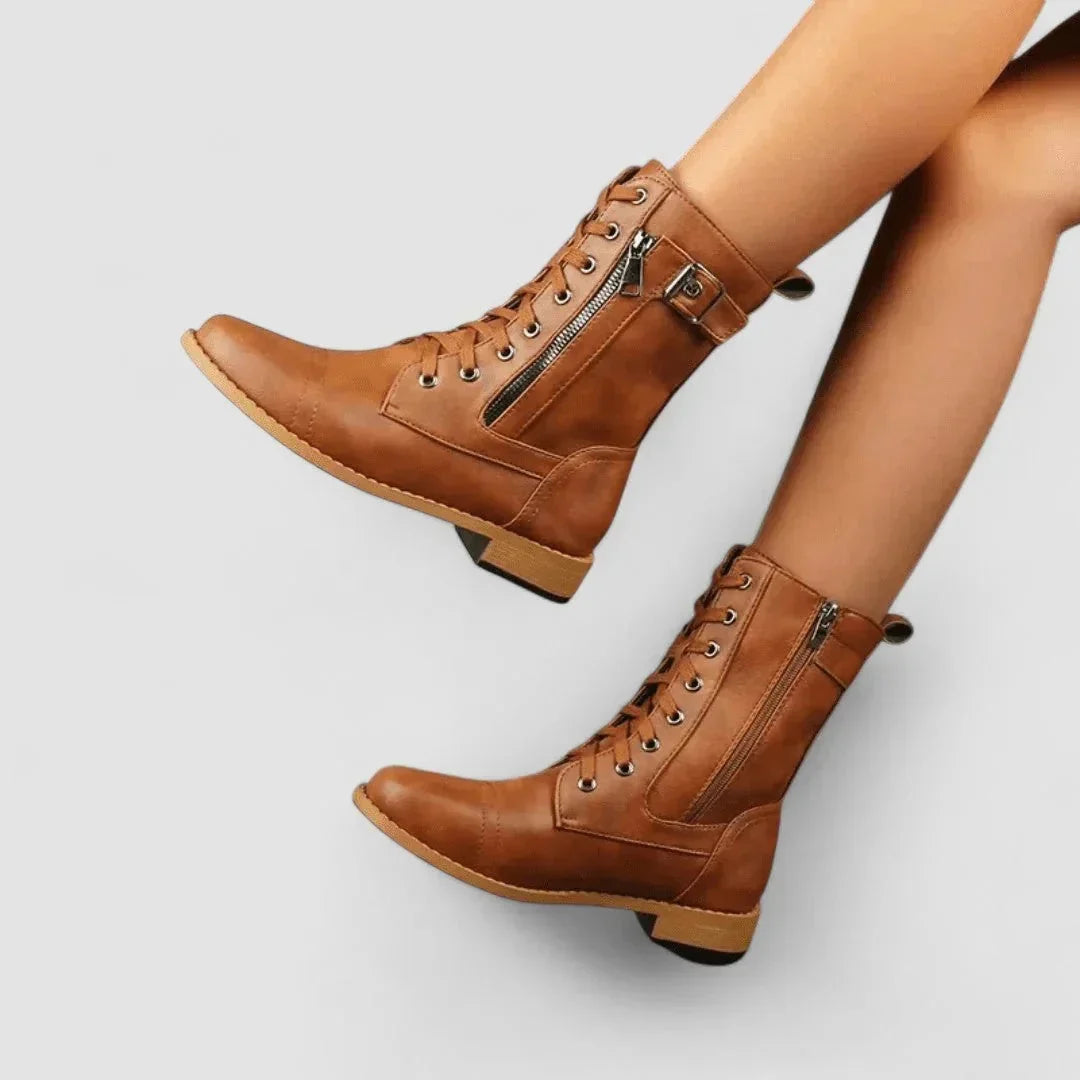 Tan grained mid-calf combat boots featuring a cap toe, lace-up front, side zip entry, and an adjustable buckle strap.