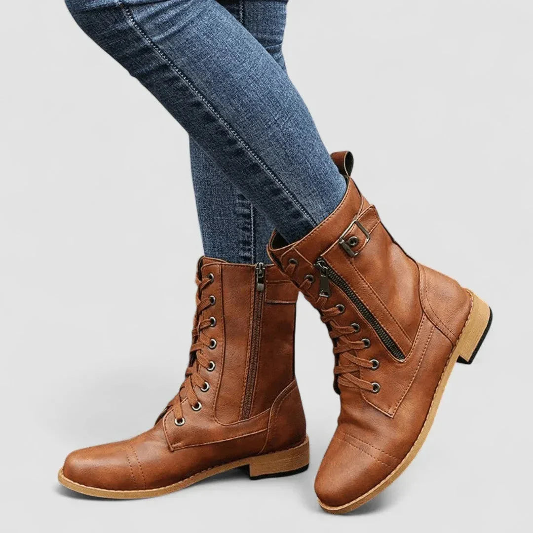 Tan grained leather mid-calf combat boots with lace-up front, side zip, cap toe, and adjustable buckle strap.