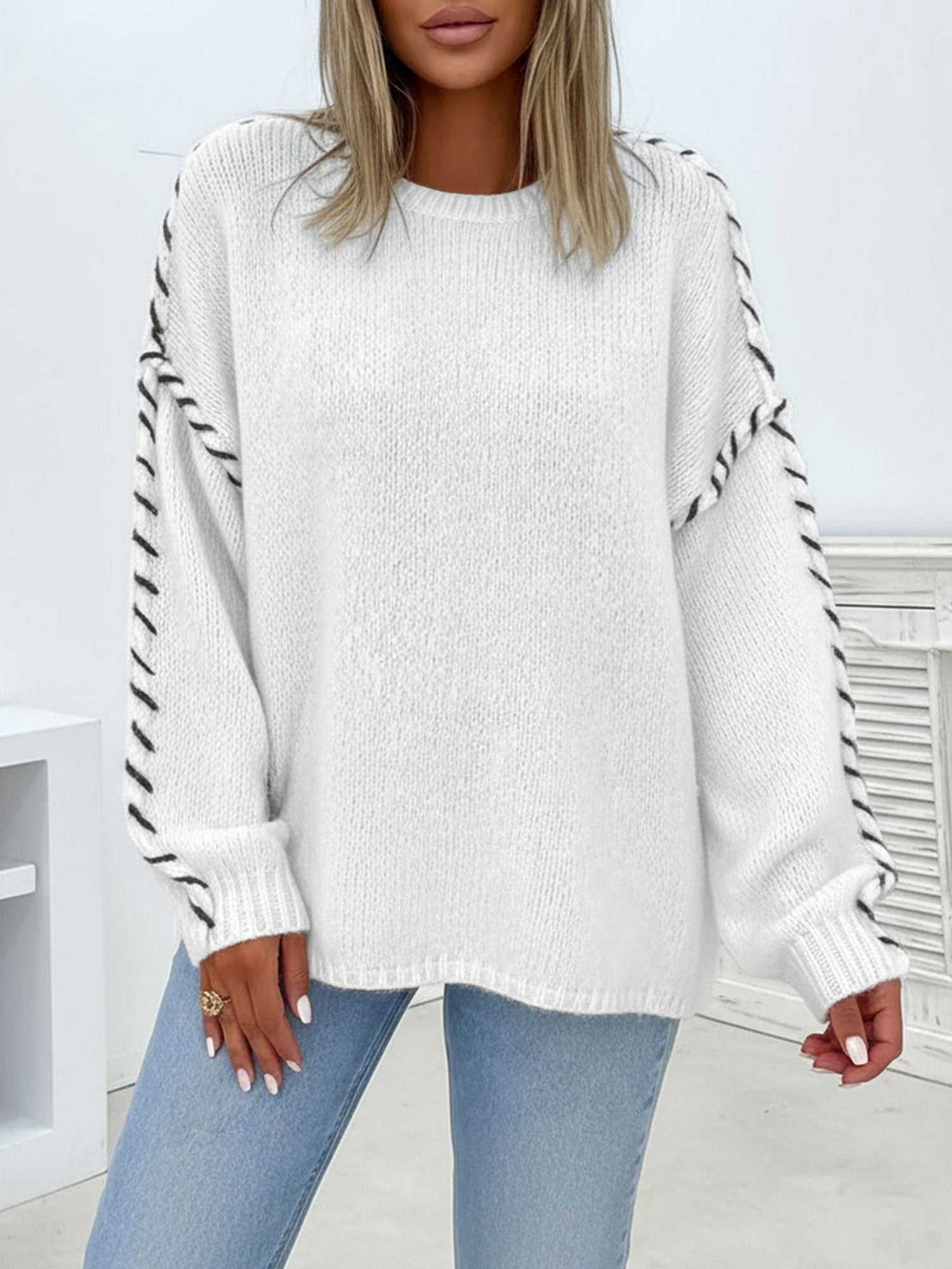 Oversized white crew-neck sweater in soft knit featuring contrast black whipstitch detailing along the sleeves.
