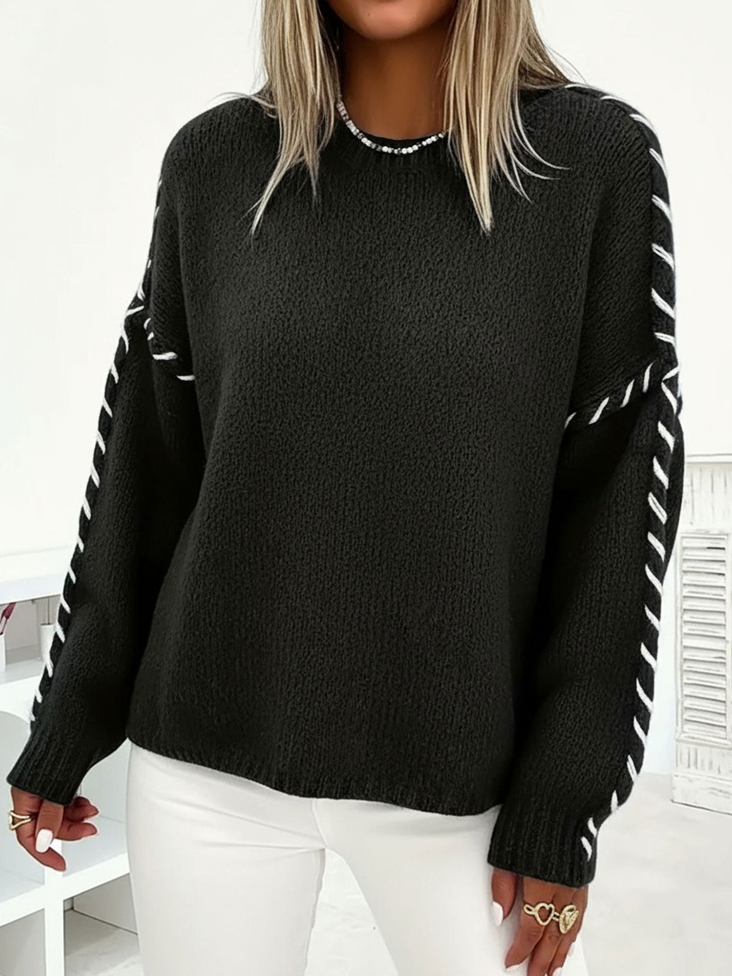 Black oversized crew-neck sweater in soft textured knit with white contrast whipstitch detailing along the sleeves.
