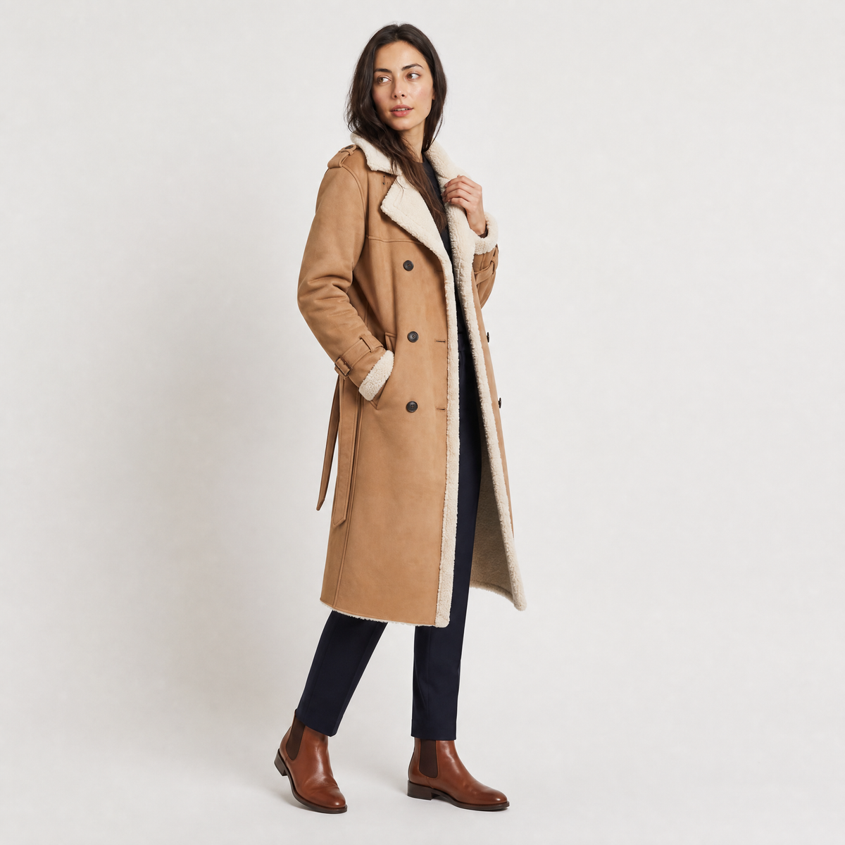 A woman wearing a tan longline leather aviator coat with borg trim and tie waist, shown in a three-quarter view
