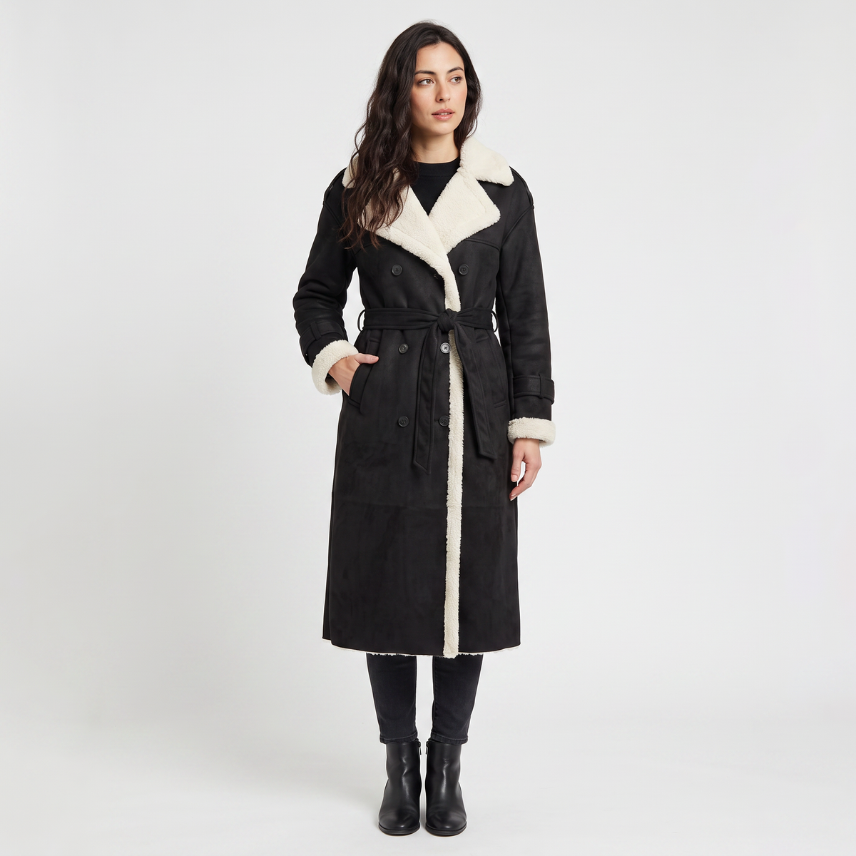 A woman wearing a black and white longline leather aviator coat with borg trim and tie waist
