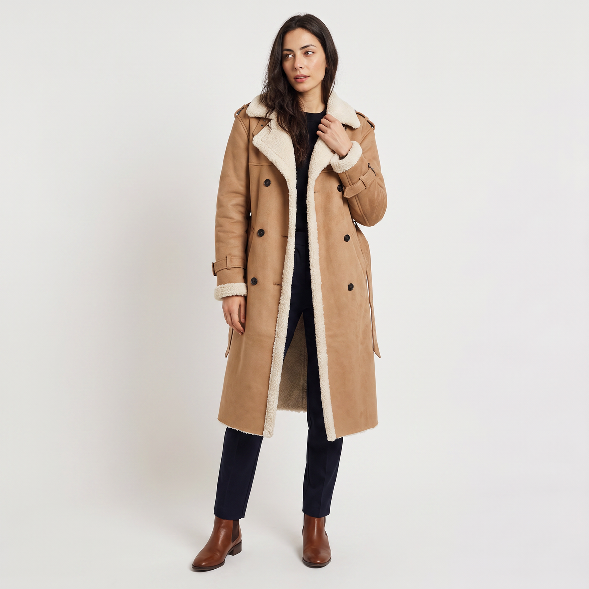 A woman wearing a tan longline leather aviator coat with borg trim, a tie waist, and double-breasted button front