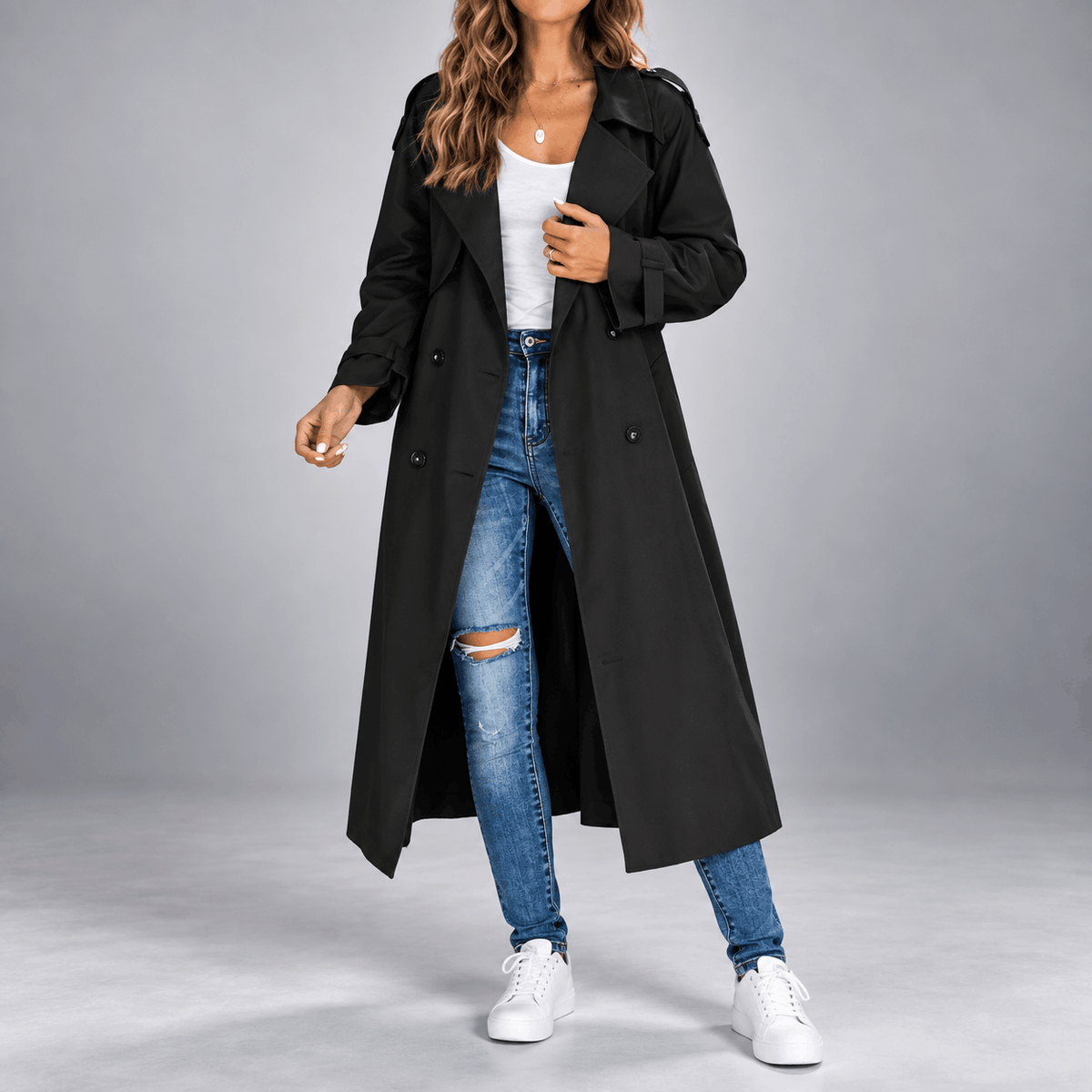 Black double-breasted longline trench coat with wide lapels, buttoned cuffs, and an oversized fit over jeans.
