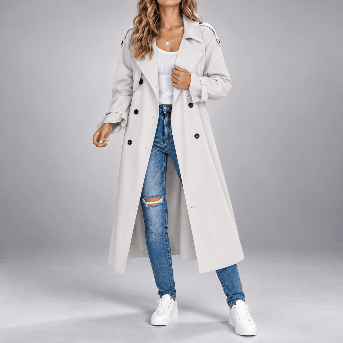 Oversized light grey longline trench coat with double-breasted buttons, wide lapels, and buttoned cuffs worn over jeans.