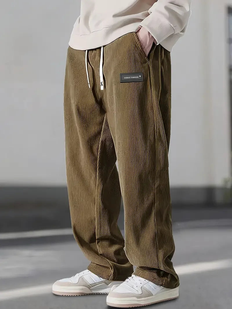 Olive green corduroy pants with a loose straight-leg fit, drawstring waist, and slant pockets worn with white sneakers.